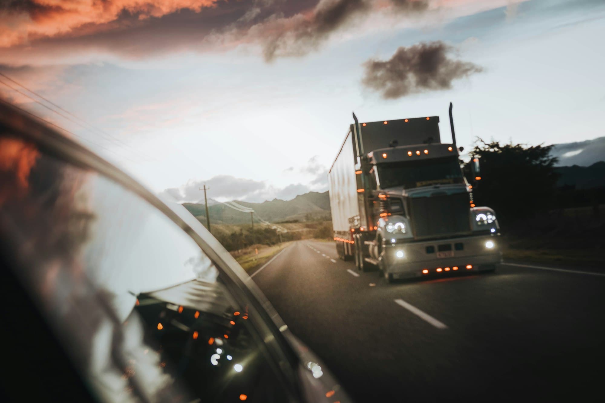 Semi truck on the highway at golden hour, seen from a truck's side mirror